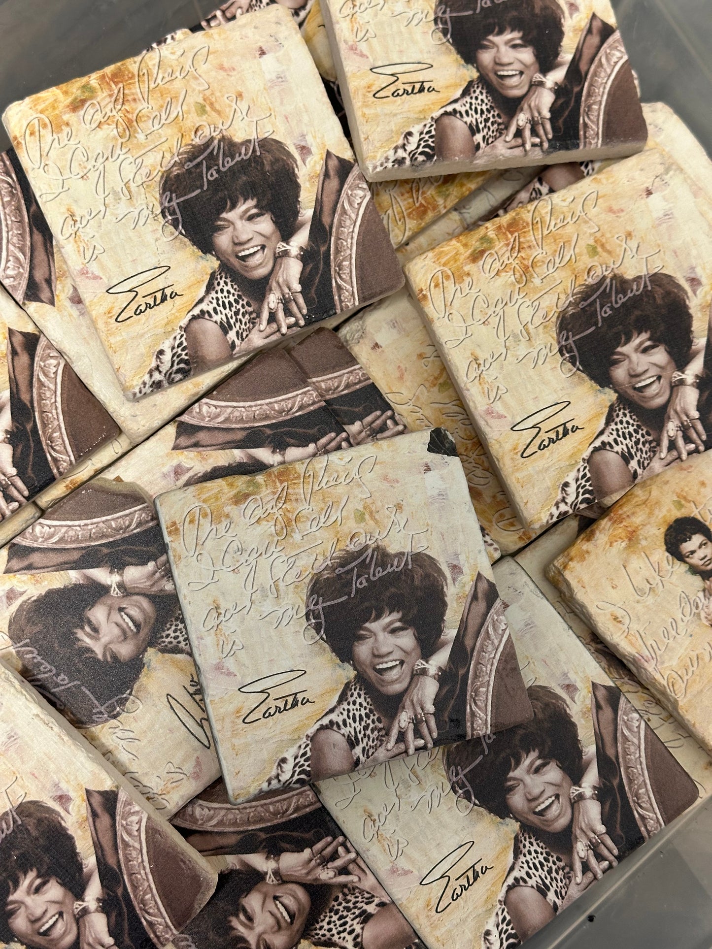 A set of Limited Edition Eartha Kitt Tumbled Stone Coasters by Simply Eartha features a black-and-white photo of Eartha, her quote “Don’t ever stop believing in yourself! - Eartha,” and a sepia-toned background.