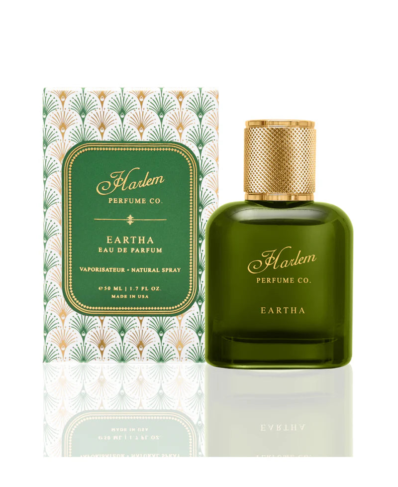 A green bottle of Simply Eartha's EARTHA EAU DE PARFUM stands before its matching green and gold Art Deco box, both featuring elegant gold lettering on a rich green background.